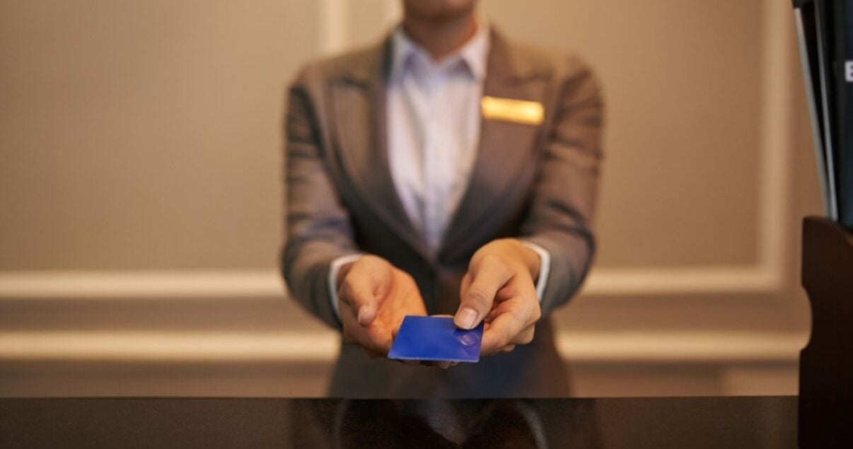 Mujer joven adulta recepcionista de hotel haciendo check in a un huesped haciendole entrega de la tarjeta de acceso a su habitacion producto de una buena gestion de revenue management