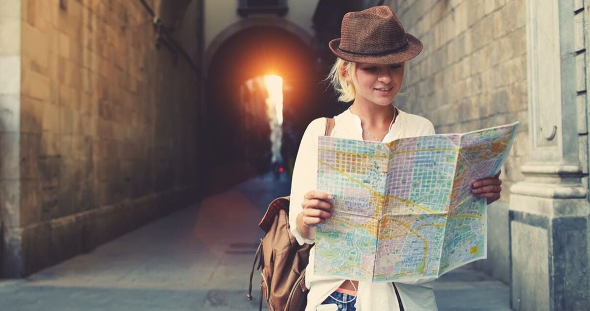 Mujer joven adulta vestida con camisa blanca y sombrero con look aventurero perdida en una ciudad europea mirando el mapa de la ciudad para llegar a su hotel donde se hospeda producto del revenue management