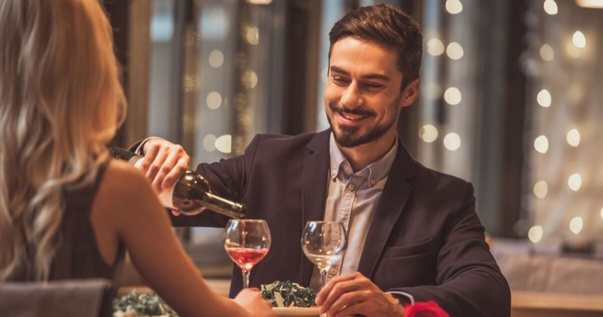 Pareja heterosexual de hombre y mujer jovenes adultos vestidos de gala para una cena romantica en el restaurante de un hotel que les regalo una botella de vino producto de una estrategia de revenue management