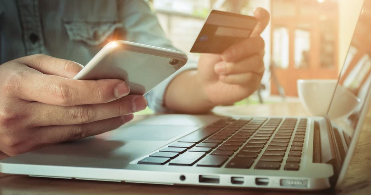 Manos de hombre joven adulto de tez blanca sentado frente a una computadora con su telefono celular y tarjeta de credito porque hara una reserva en un hotel que vende a traves de otas como resultado de su gestion de 