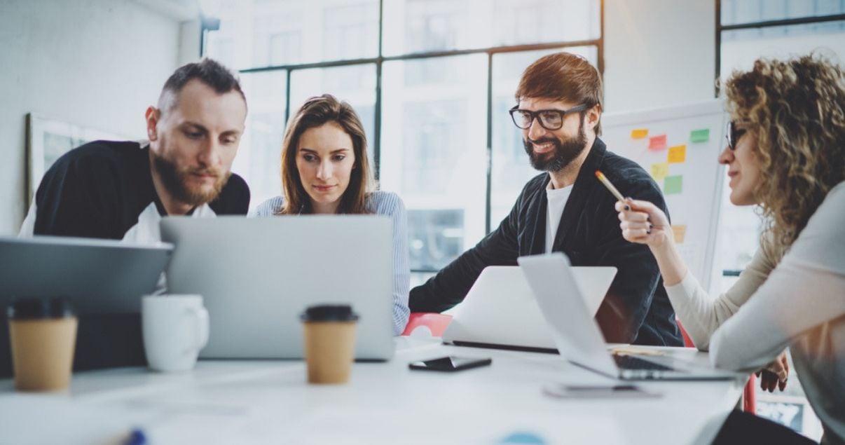 Equipo de revenue management de un hotel conformado por dos hombres y dos mujeres jovenes adultos sentados frente a una laptop haciendo un analisis de los datos que arrojo el ultimo reporte de revenue management del 