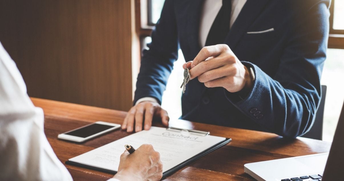 Manos de hombre joven adulto sobre el escritorio de recepcion del hotel en el que realiza revenue management haciendo check in a un huesped que firma planilla con lapicera negra