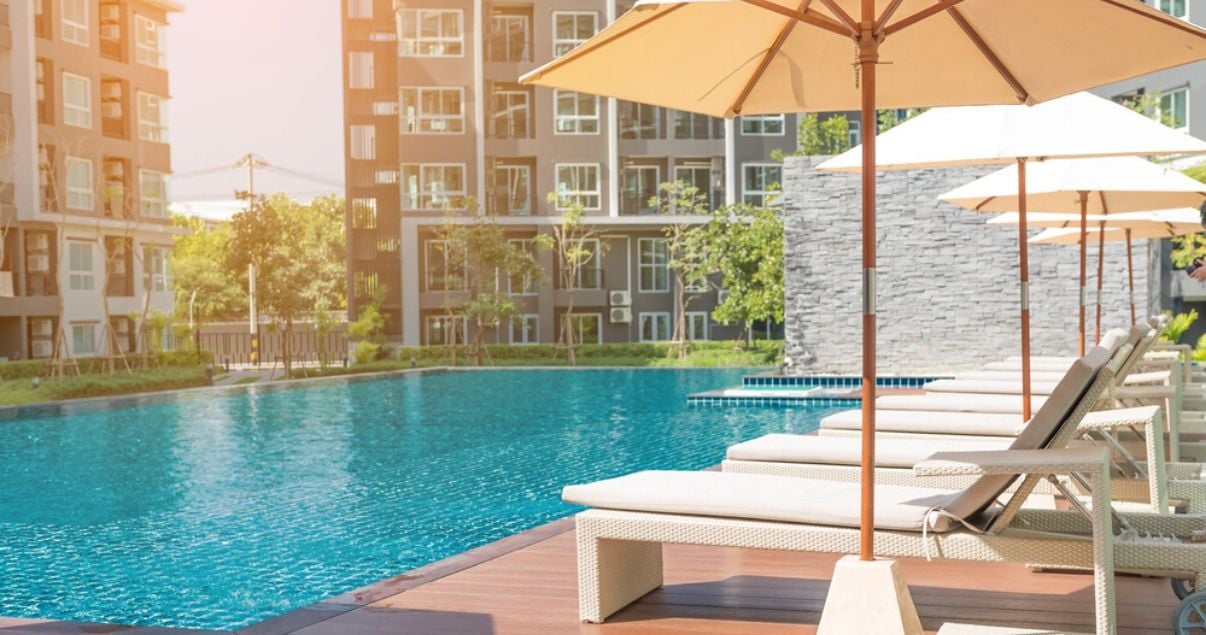 Plano general de una fotografia de un articulo sobre hoteles con piscina con una piscina olimpica de agua limpia con las habitaciones de fondo y reposeras blancas con sombrillas blancas