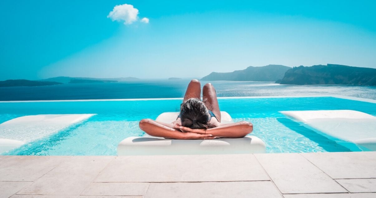 Primer plano de una mujer joven adulta de cabello castano posando para produccion de un articulo sobre hoteles con piscina mostrandose muy relajada en el agua de la piscina de su habitacion con vista al mar de rio de