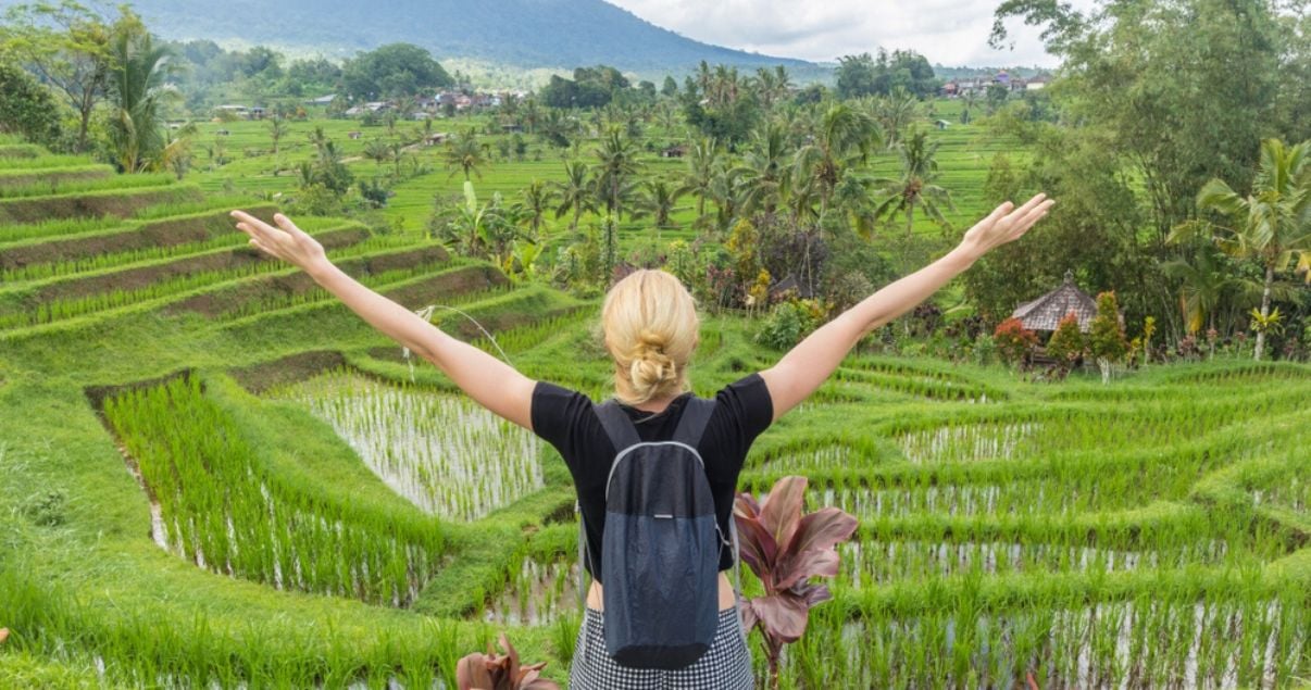 Mujer joven adulta rubia de tez blanca vestida en shorts parada de espaldas levantando los brazos como abranzando el fondo de plantas y naturaleza dentro de uno de los hoteles sustentables asiaticos