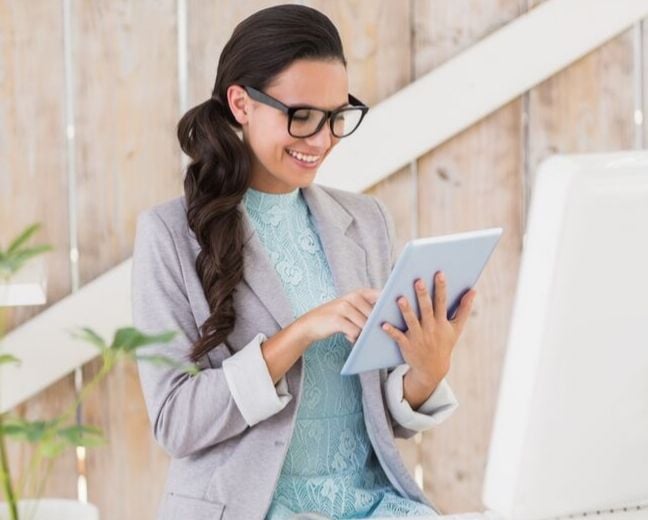 Mujer joven adulta parte del personal de un hotel trabajando en recepcion sonriendo mientras mira su ipad y gestiona reservas facilmente a traves de un channel manager