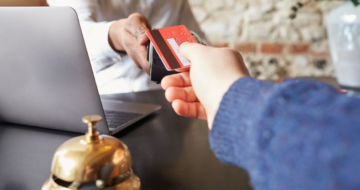 Manos de hombre joven adulto sobre la mesa de recepcion haciendo check in para alojarse y abona con tarjeta de credito como forma de pago en hoteles