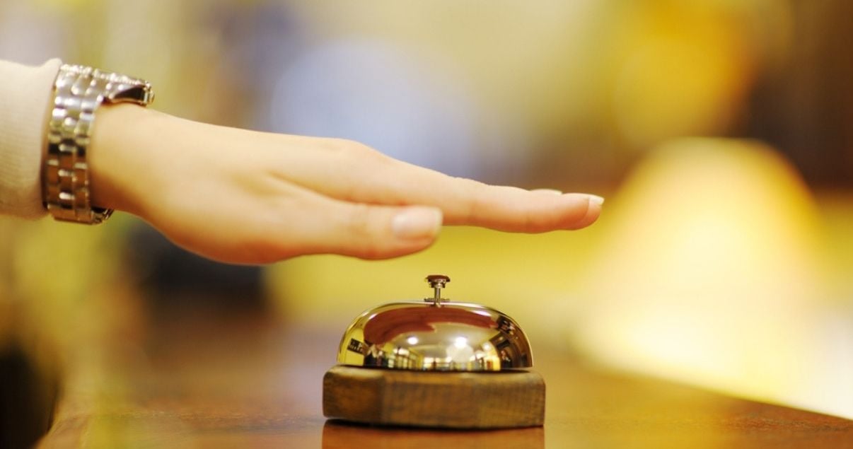 La mano de una mujer joven adulta que viste un reloj y esta a punto de tocar la campanilla de un Hotel para solicitar ayudar de su personal, llego al hotel gracias a la gestion de revenue management